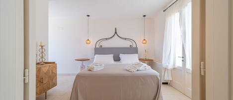 A neatly arranged bedroom with a bed, bedside tables, a wooden cabinet, and hanging pendant lights.