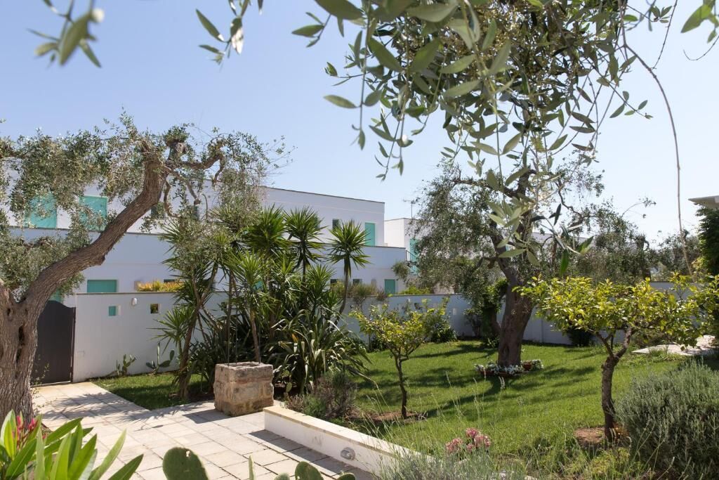 Un patio con un edificio blanco, varios árboles y un césped bien cuidado.