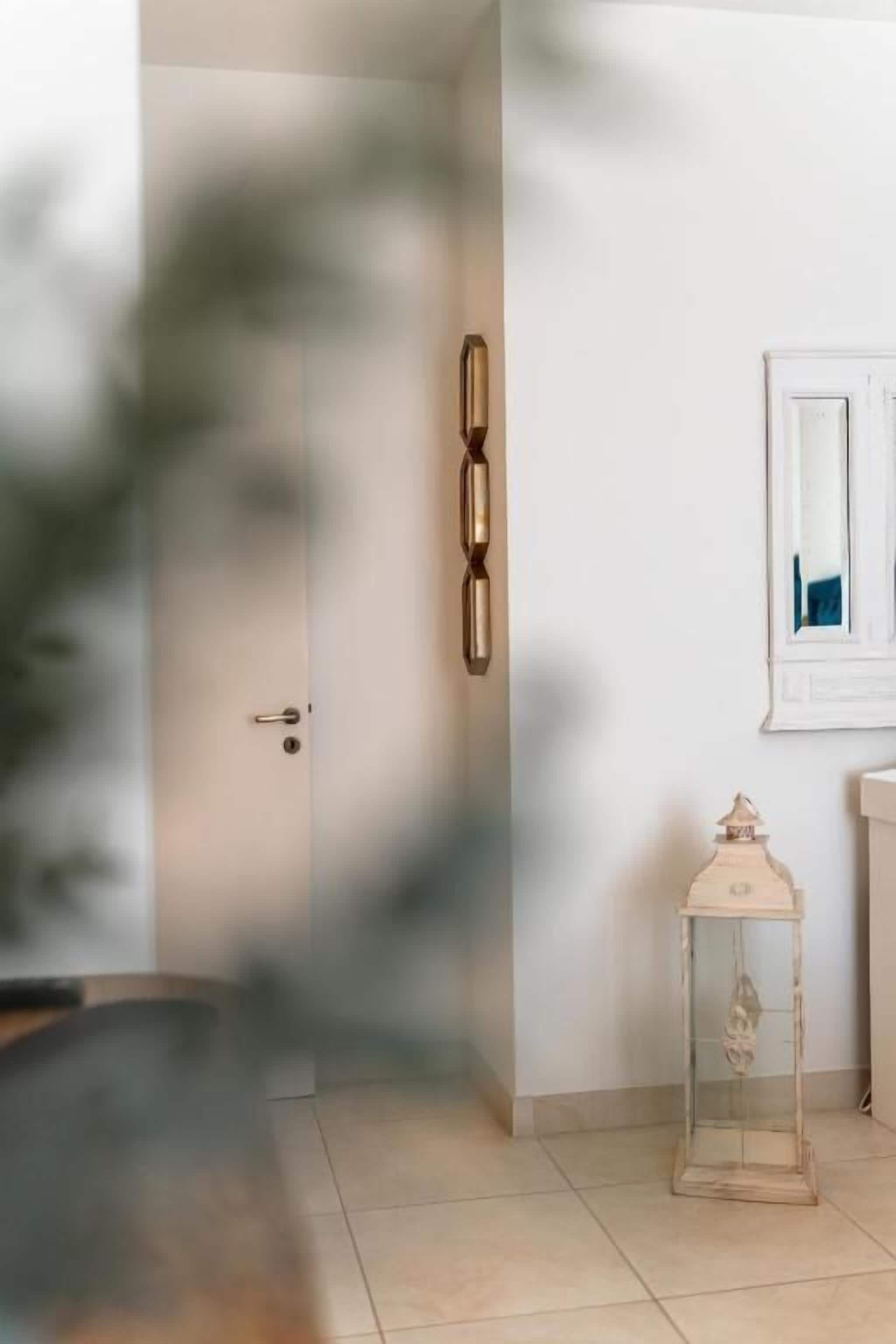 En gang med en dør, en vægmonteret lampe og et lille bord med en pyntgenstand.