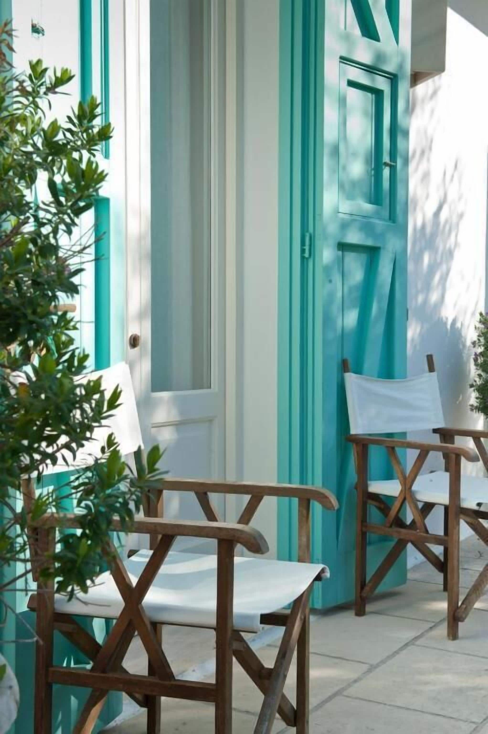 An outdoor seating area with wooden chairs and a white table, a turquoise door, and a potted plant.
