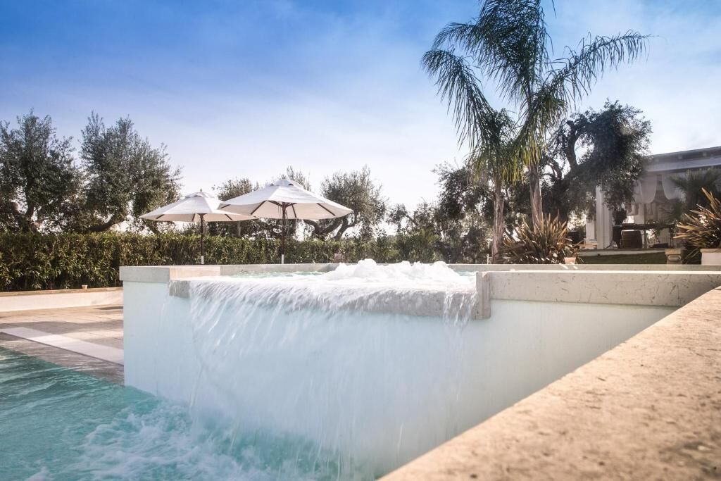 Una piscina con cascada, rodeada de palmeras y sombrillas.
