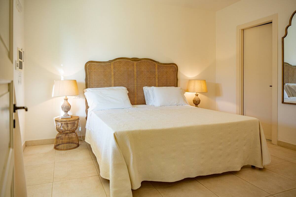 A neatly made bed with a textured bedspread, two bedside lamps, and a wicker nightstand.
