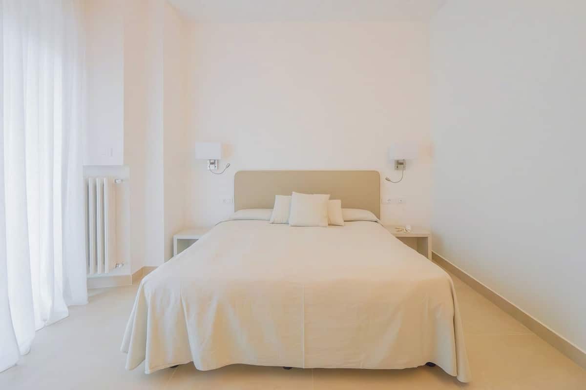 Een minimalistisch hotelkamer met een groot bed, nachtkastjes en een radiator.