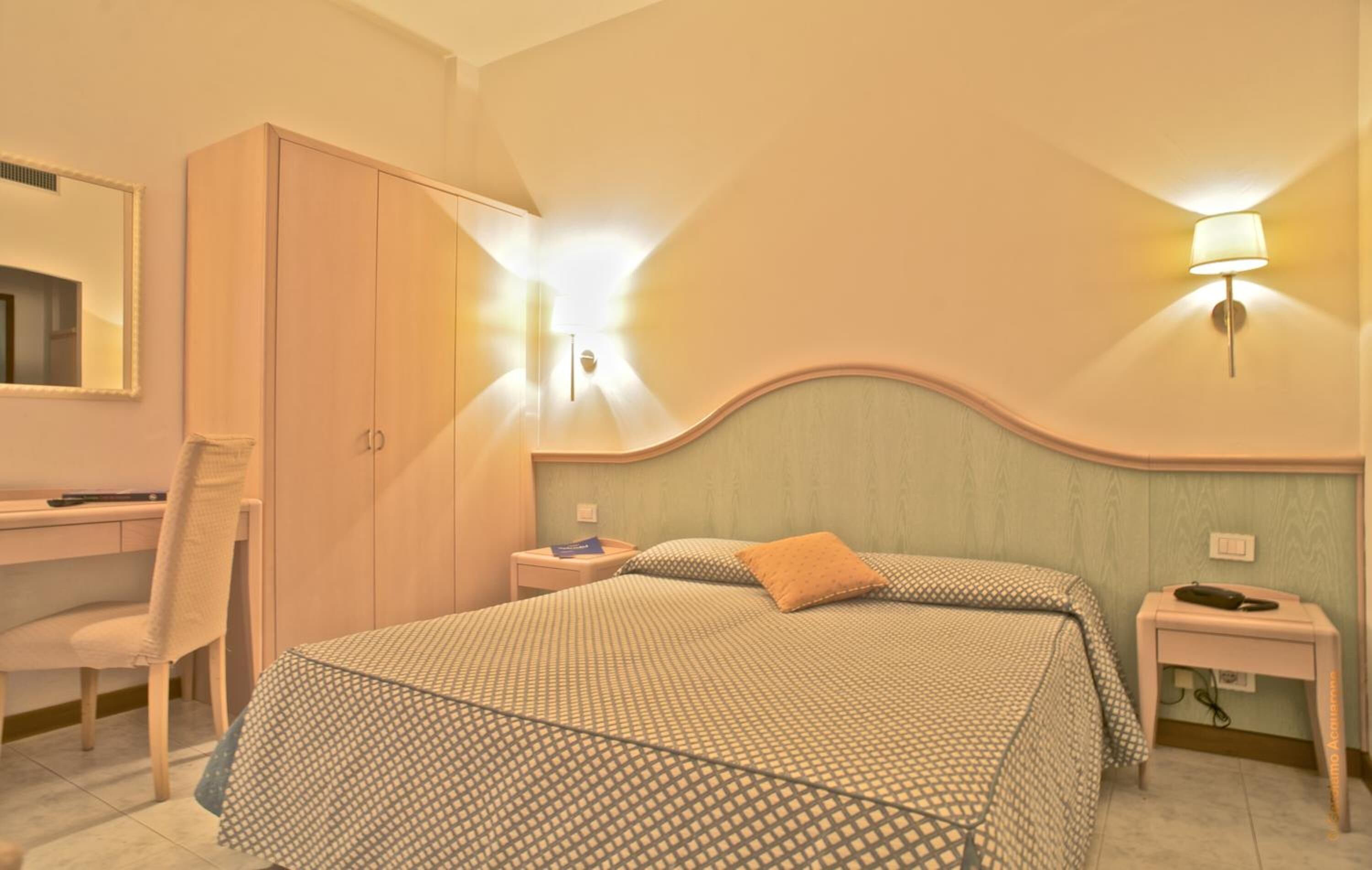 Ein Hotelzimmer mit einem Bett, einem Schreibtisch, einem Stuhl, einem Kleiderschrank und zwei Wandleuchten.