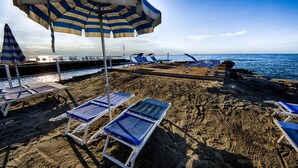A beach with striped umbrellas, lounge chairs, and a pier in the background. - Hotel Splendid (Diano Marina)