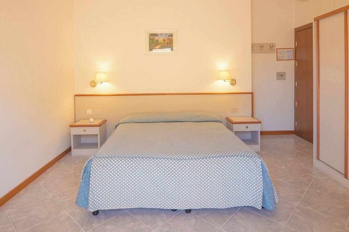 Een slaapkamer met een bed, twee nachtkastjes, een wandairconditioner en een klein schilderij.