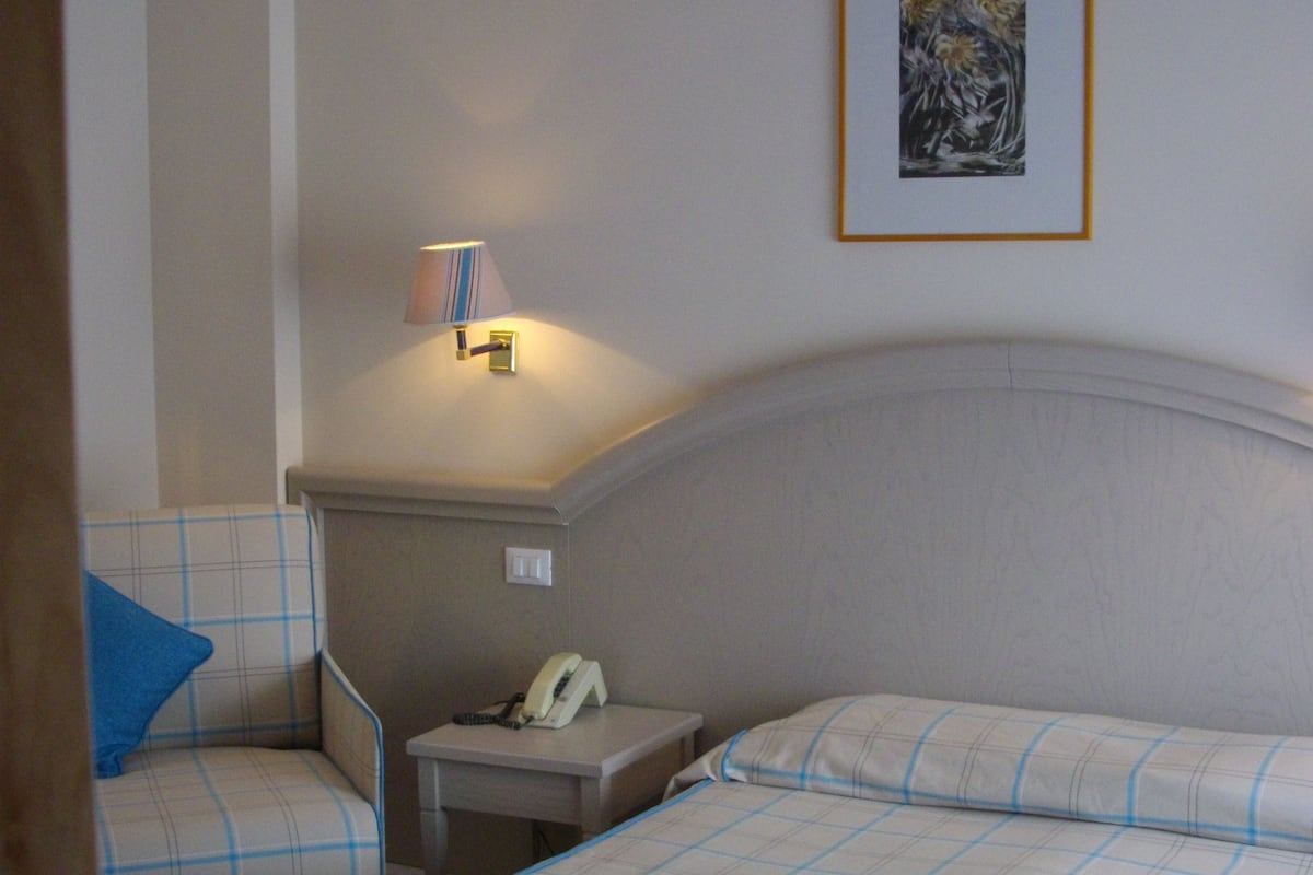 Een hotelkamer met twee bedden, een nachtkastje, een lamp en een ingelijst foto aan de muur.