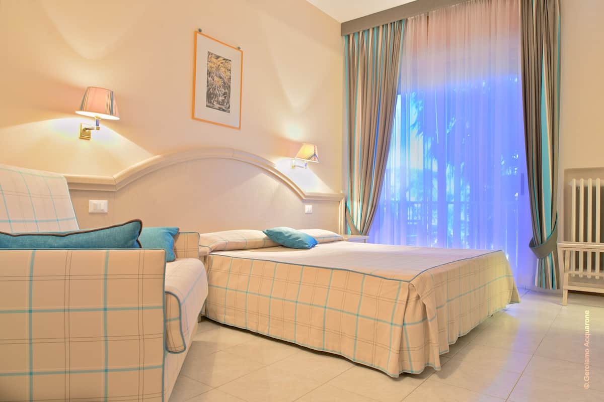 Een hotelkamer met een bed, een stoel, een nachtkastje en een raam met gordijnen.