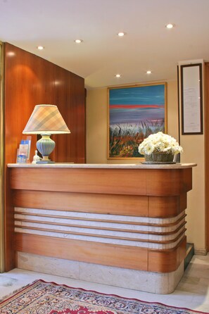 A reception desk with a lamp, a floral arrangement, and a painting on the wall.