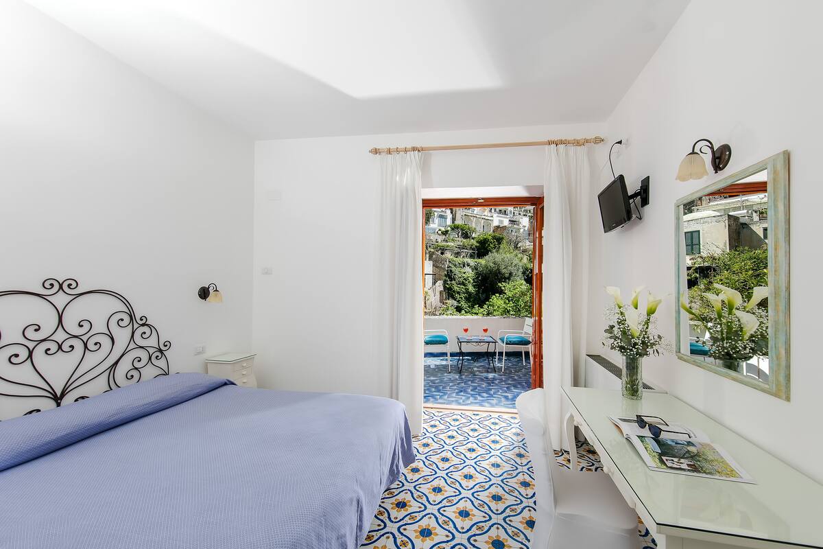 A bedroom with a bed, a desk, a mirror, and a view of a courtyard.