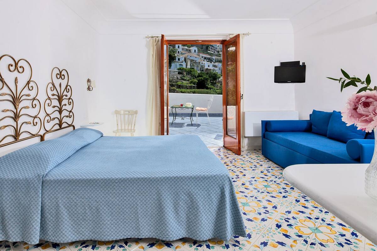 A hotel room with a bed, a blue sofa, a TV, and a view of the outside.
