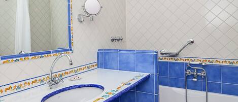 Un baño con lavamanos, espejo y bañera, con azulejos azules y blancos con motivos florales.