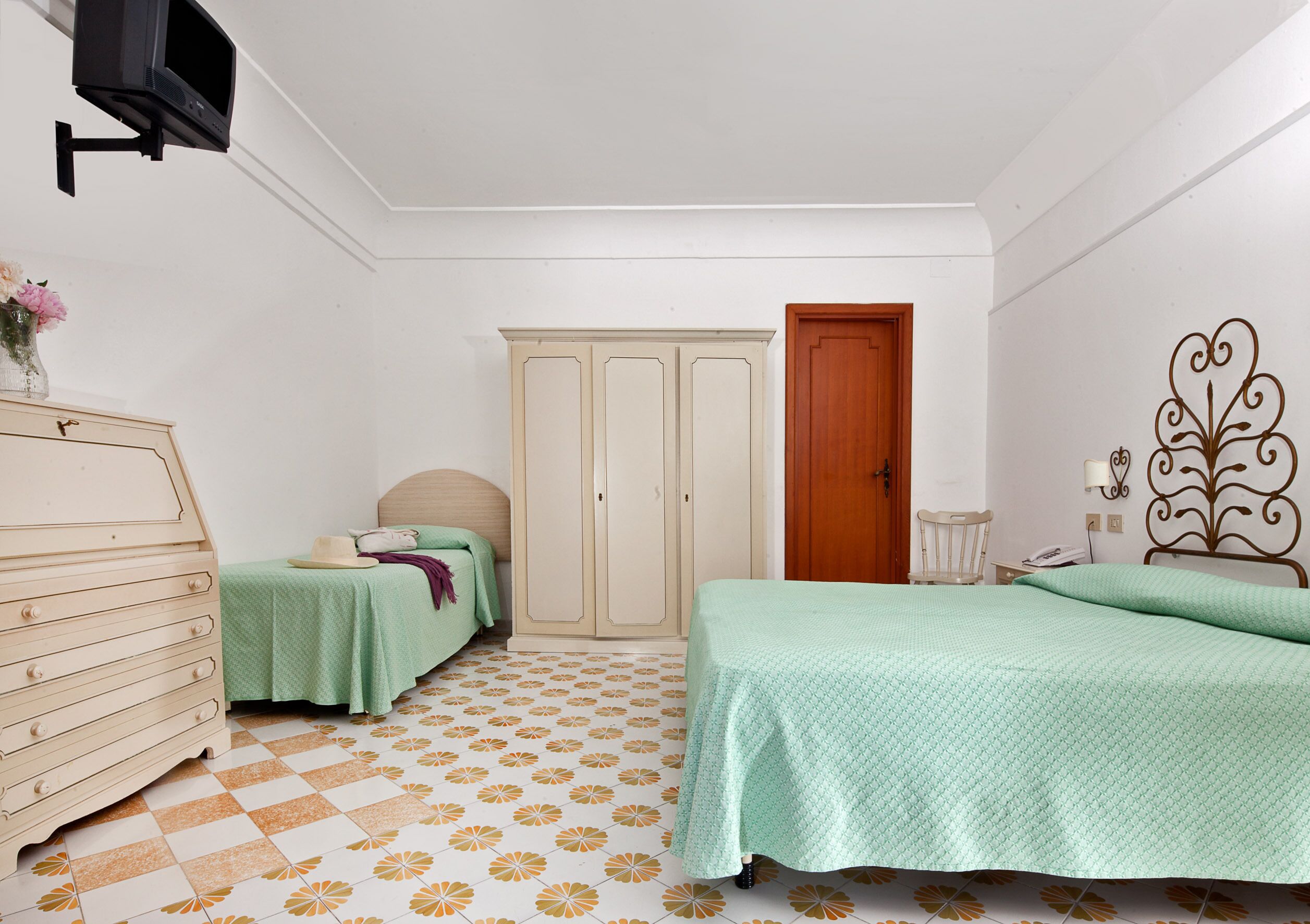 A bedroom with a bed, dresser, wardrobe, and a television mounted on the wall.