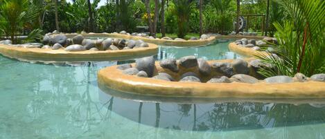 A clear pool with circular stone borders and tropical vegetation around it.