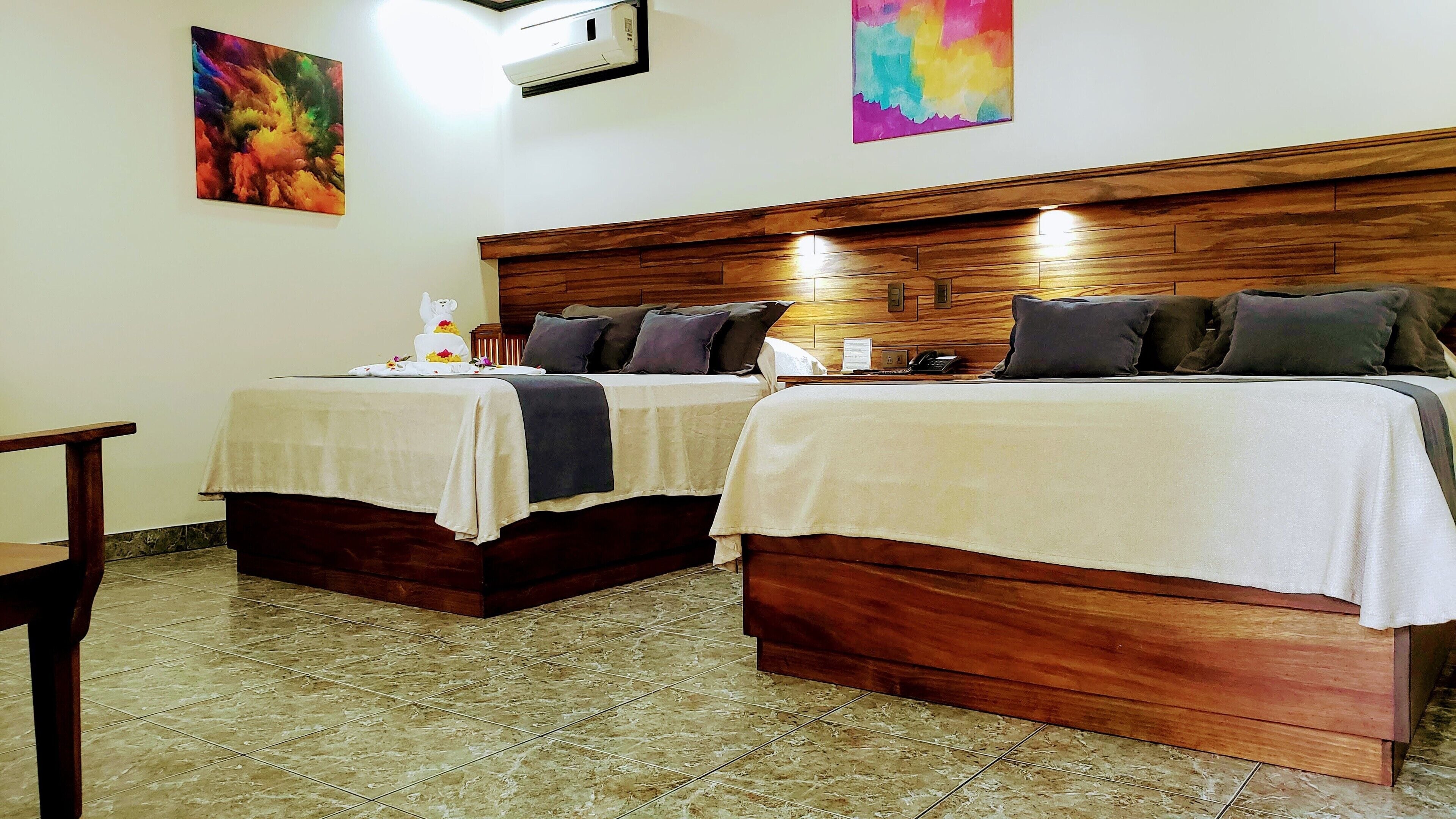 Deux lits simples avec des têtes de lit en bois, une table de chevet et un climatiseur fixé au mur.