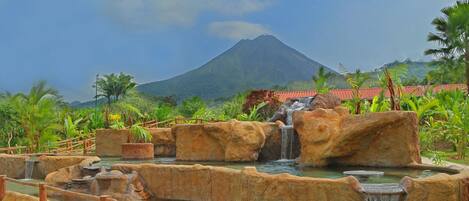 A landscaped garden with a waterfall, a mountain in the background, and a red-roofed building.