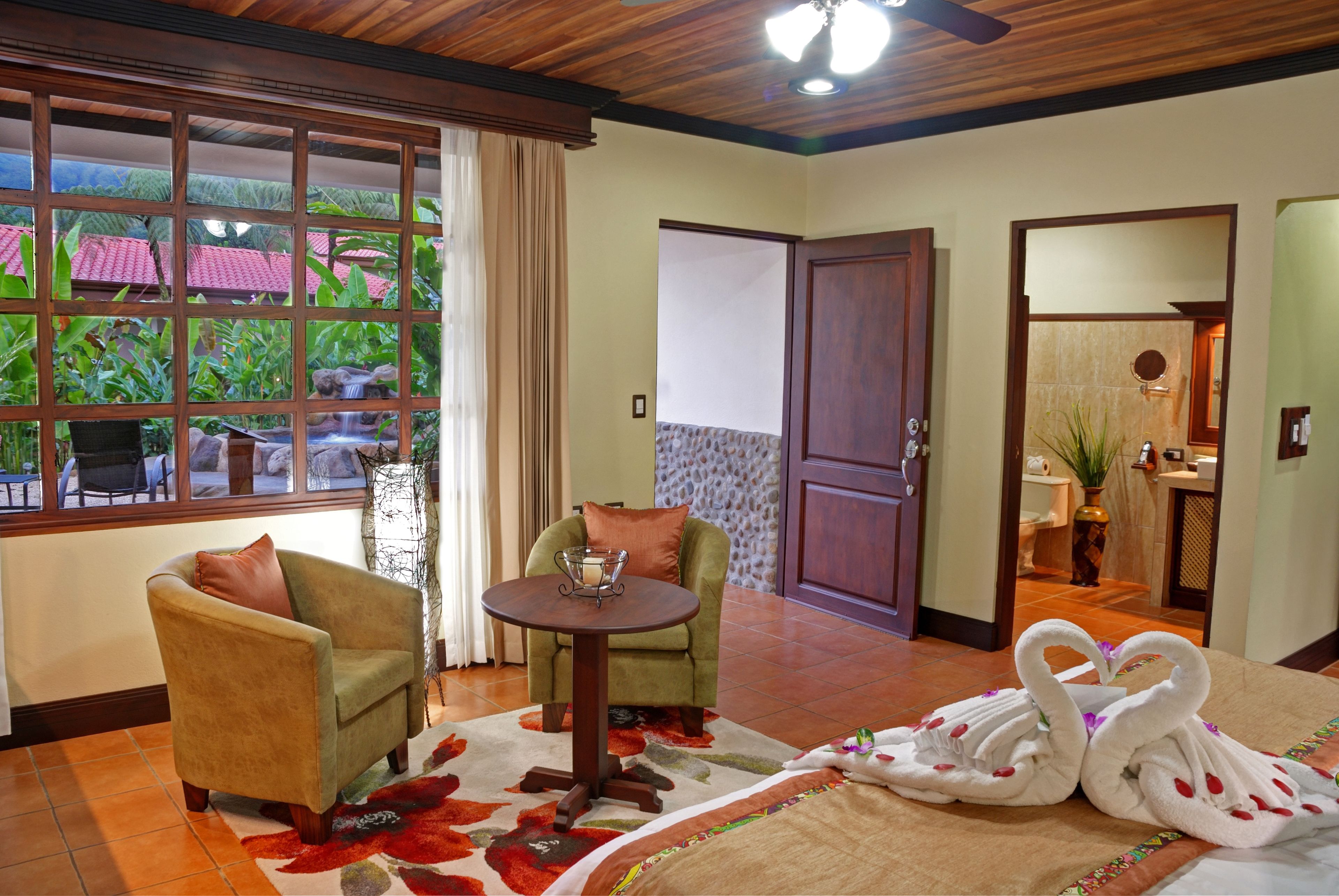 A room with two armchairs, a small round table, and a bed with swan-shaped towels.
