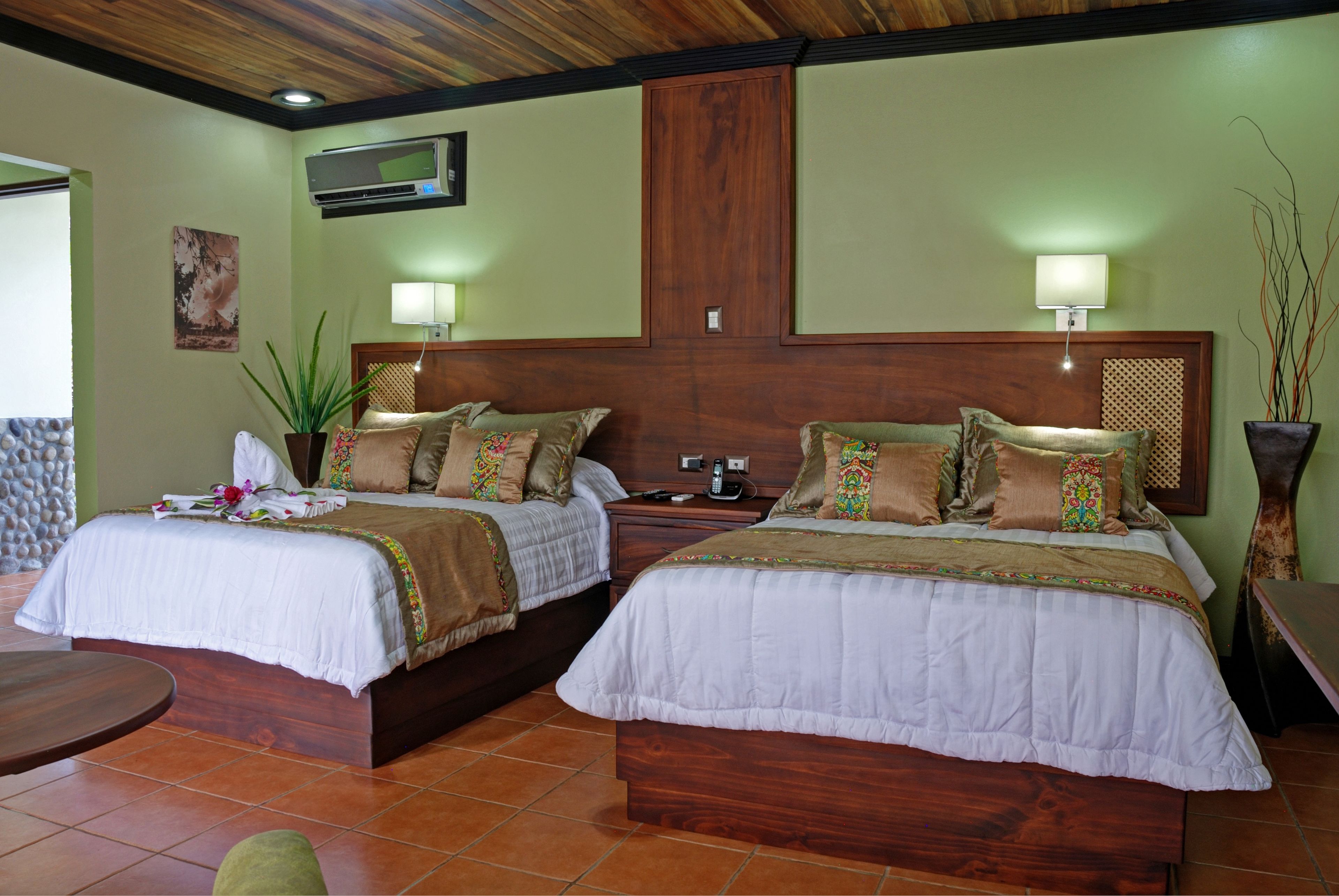 A hotel room with two beds, a wooden headboard, a TV, a lamp, and a potted plant.