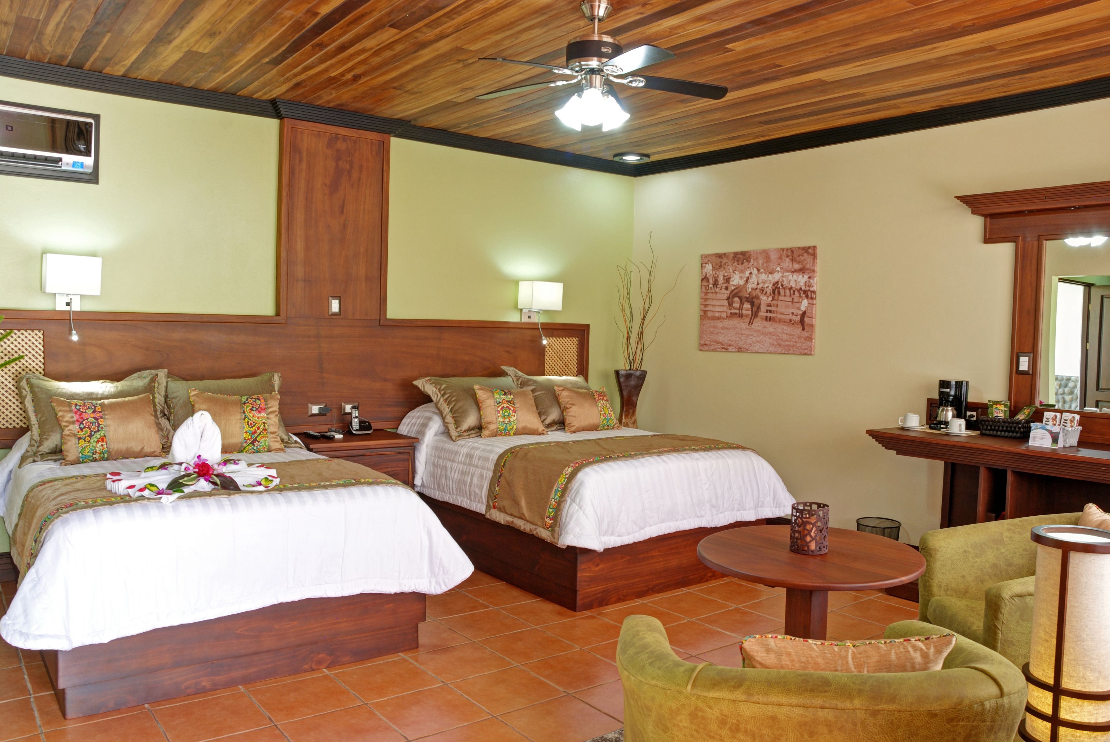 Habitación de hotel con dos camas, ventilador de techo, una mesita y una silla.
