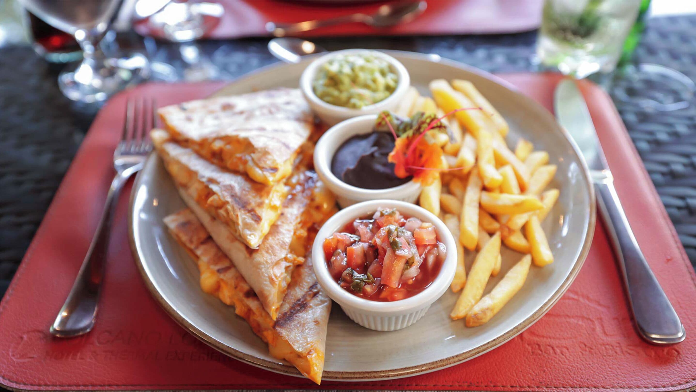 A plate with a sandwich, French fries, and two small bowls of sauces.