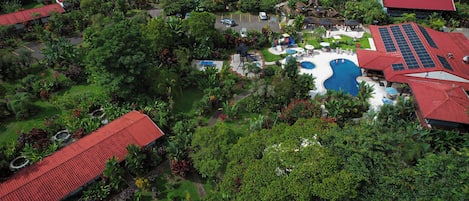 Luchtbeeld van een resort met meerdere gebouwen, een zwembad en weelderige begroeiing.