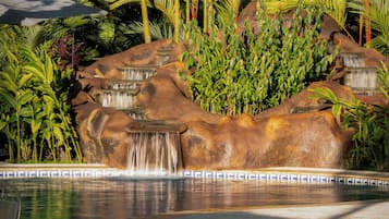 A rock waterfall feature with a pool in front, surrounded by tropical plants.
