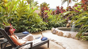 Relax in a serene outdoor oasis surrounded by lush tropical plants and a soothing water feature.
