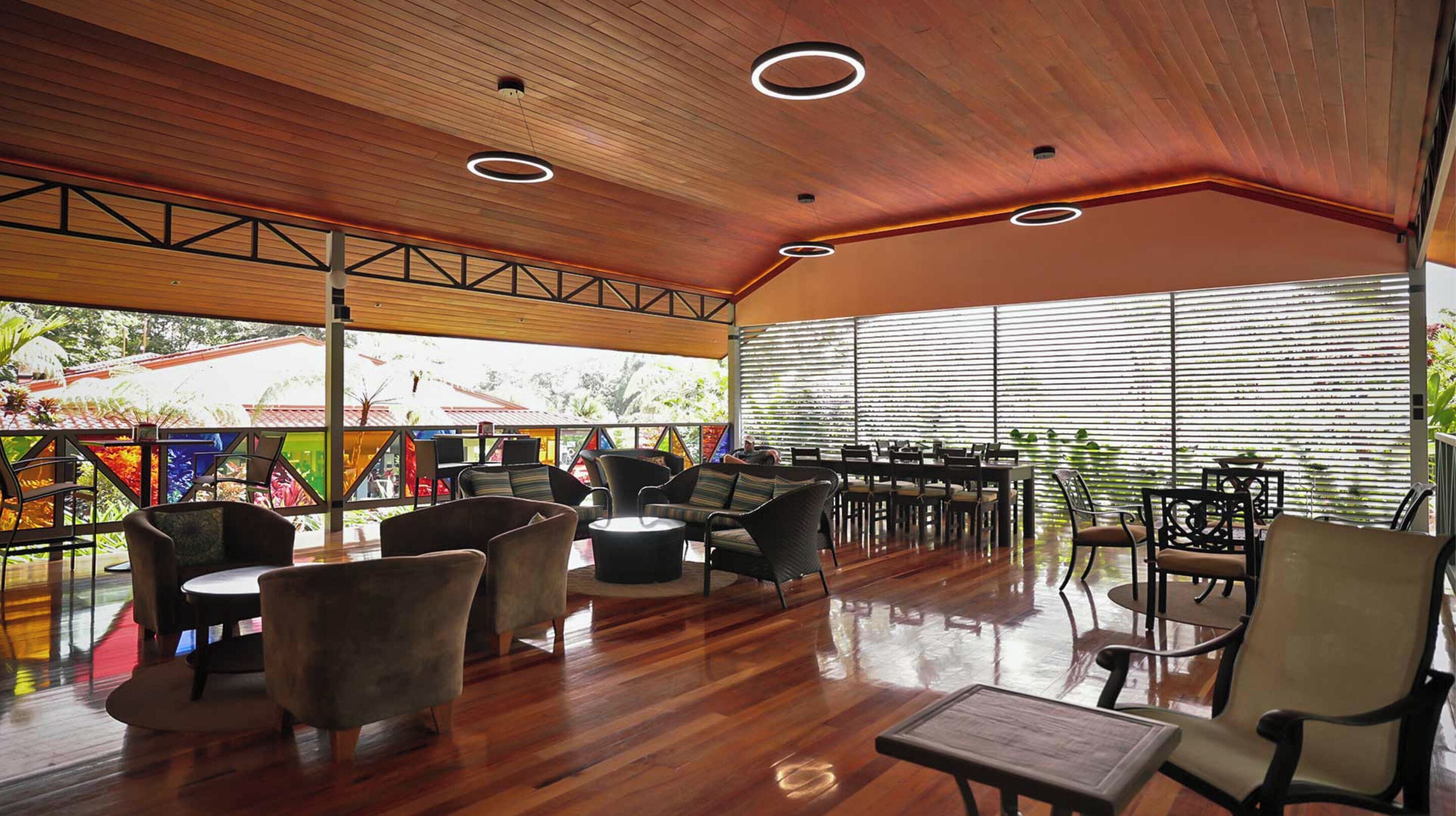 A spacious indoor area with wooden flooring, multiple seating arrangements including sofas and chairs, and large windows providing natural light.