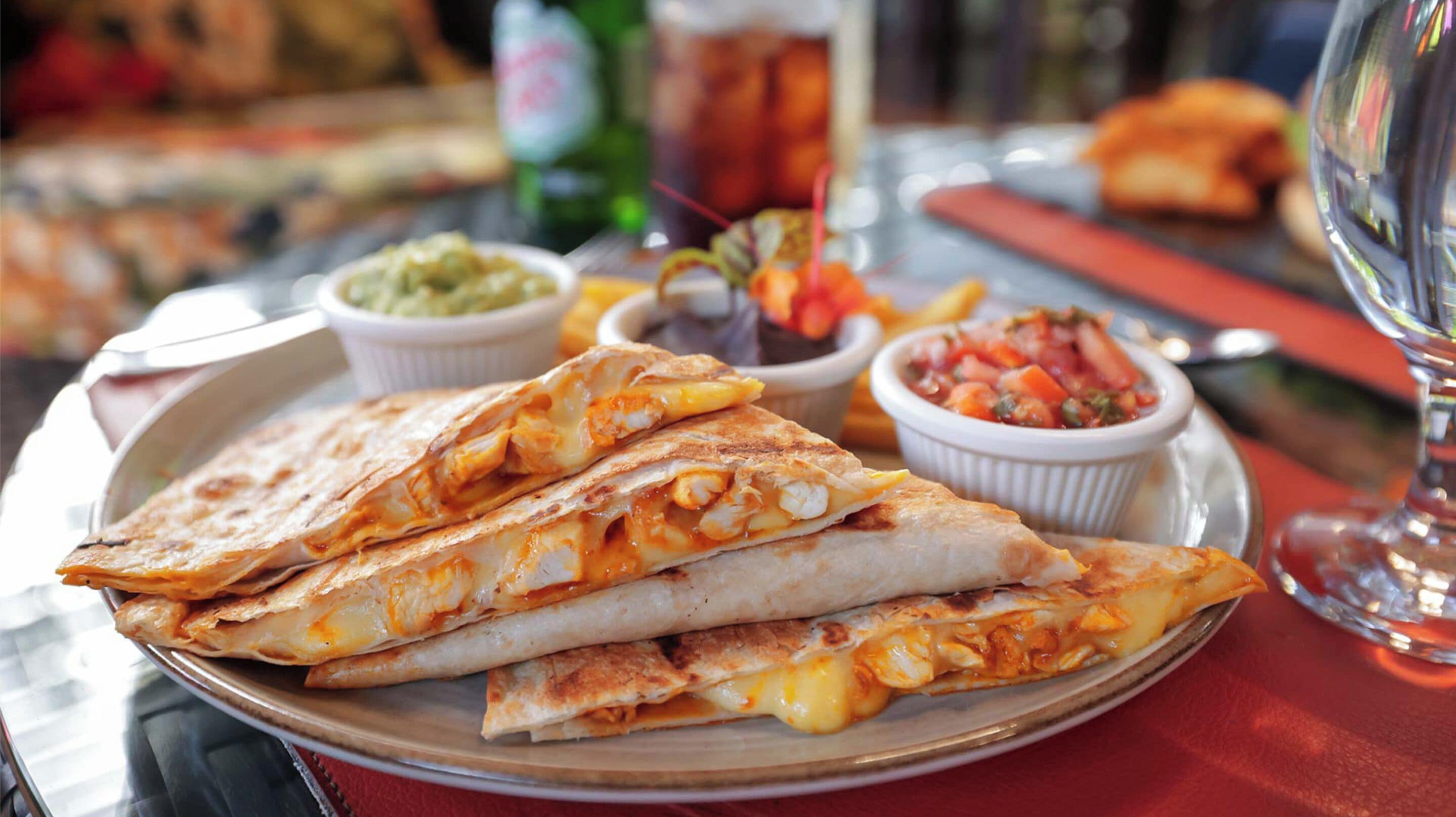 A plate of quesadillas with cheese, a small bowl of guacamole, and a side of salsa.