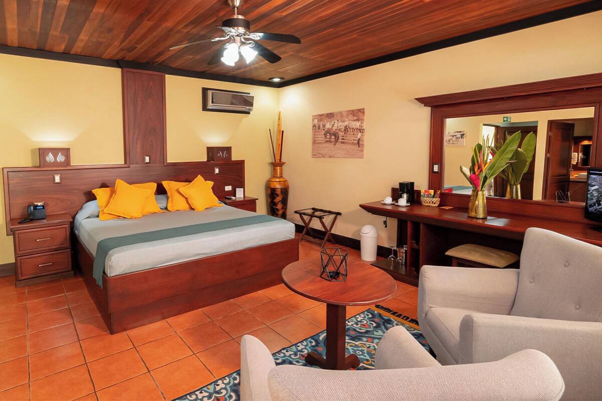 Une chambre d’hôtel avec un plafond en bois, un lit avec des oreillers orange, un bureau avec un ordinateur et une chaise.