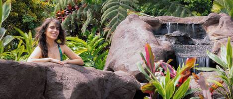 A woman sitting on a rock by a waterfall in a lush garden.