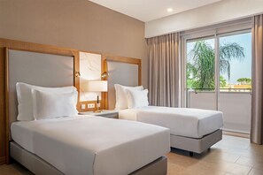 A hotel room with two beds, a large window with curtains, and a view of greenery outside. - Wyndham Grand Algarve Quinta do Lago (Loulé)