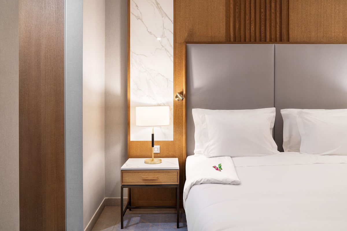 A hotel room with a bed, a nightstand with a lamp, and a marble wall.