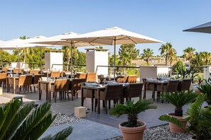 An outdoor dining area with wicker tables and chairs, large umbrellas, and potted plants. - Wyndham Grand Algarve Quinta do Lago (Loulé)