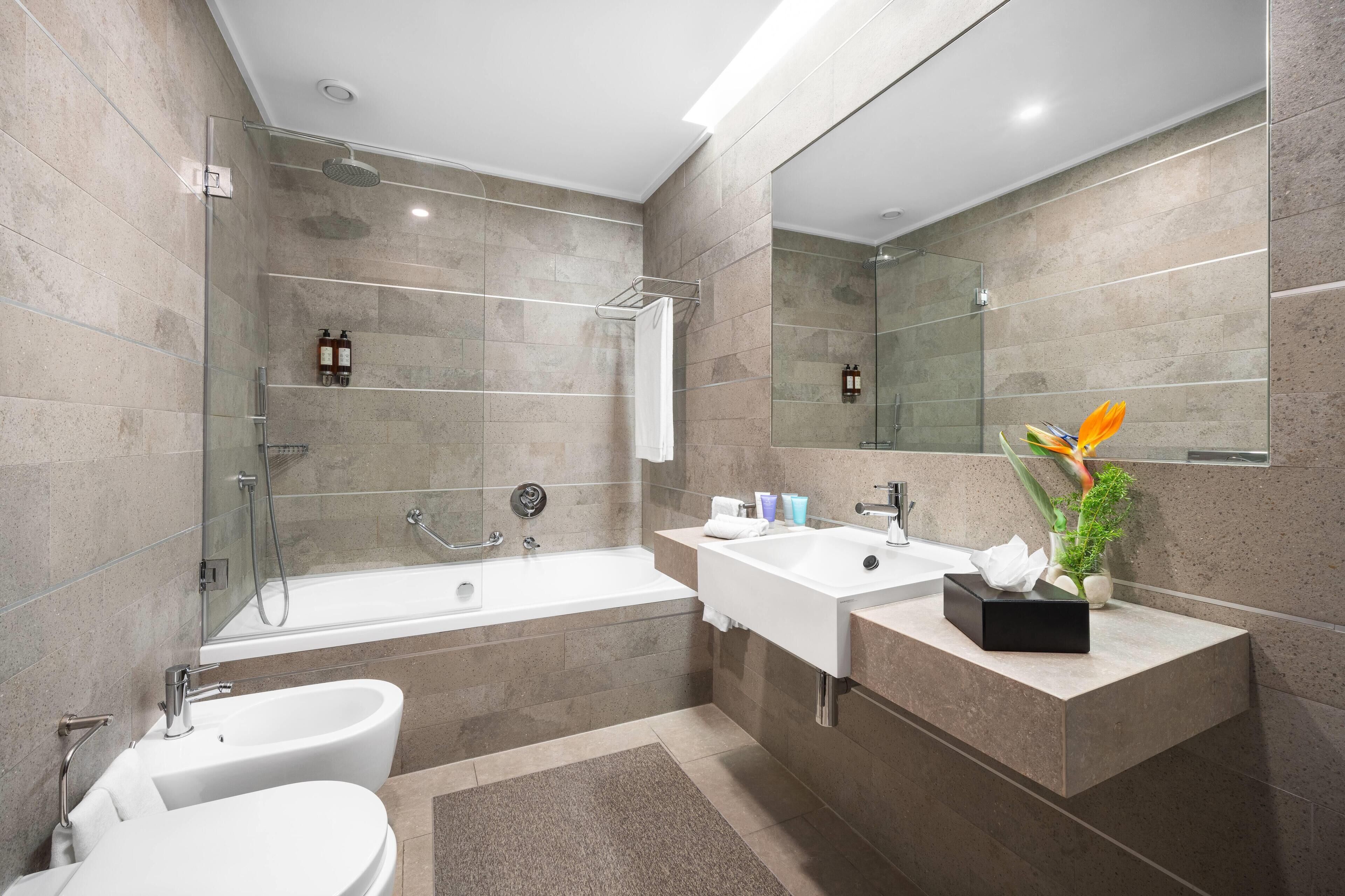 A modern bathroom with a bathtub, a double sink, a toilet, and a glass-enclosed shower.