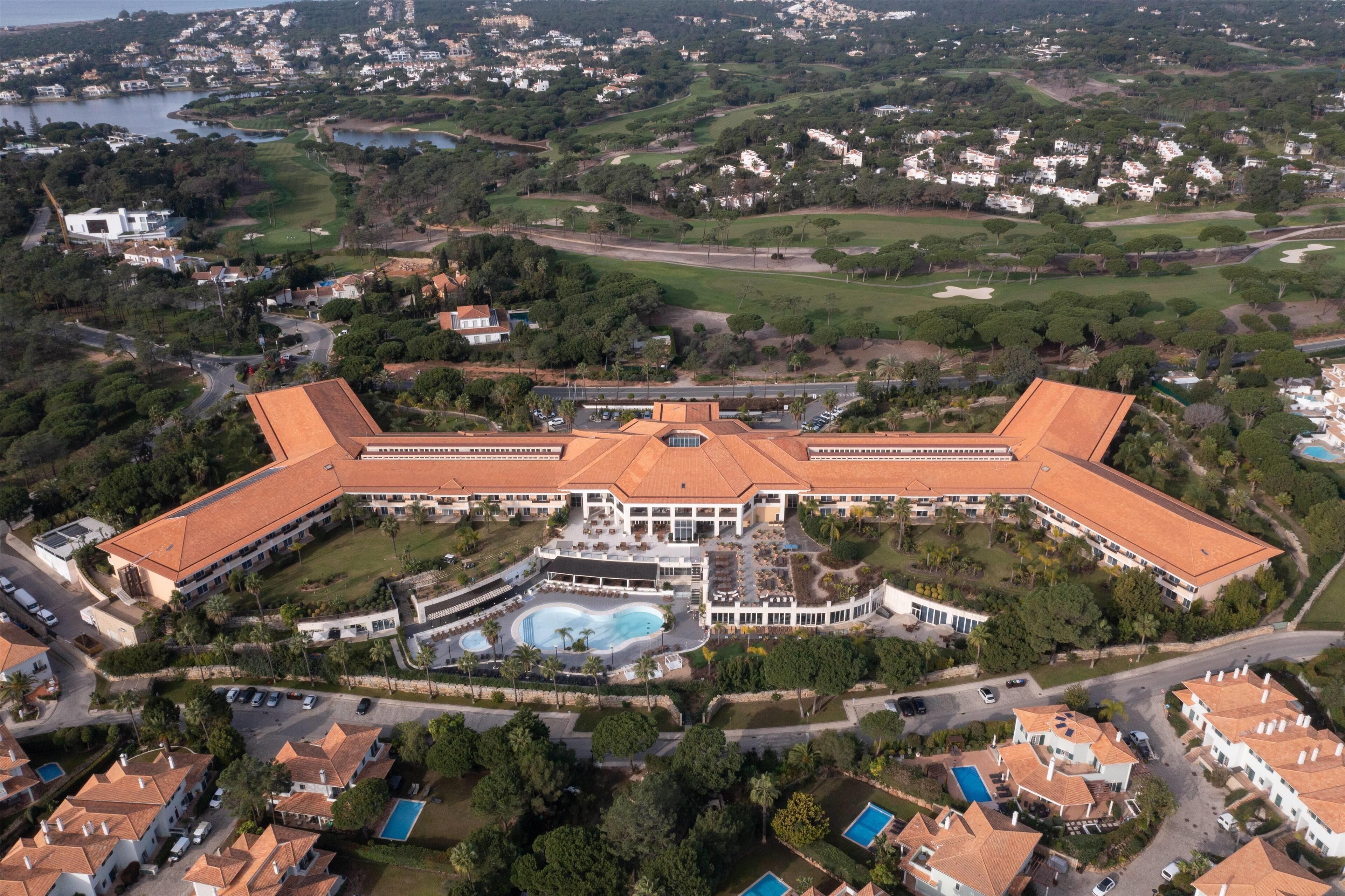 Vista aérea de un gran complejo turístico con piscina central, varias villas para huéspedes y campos de golf circundantes.