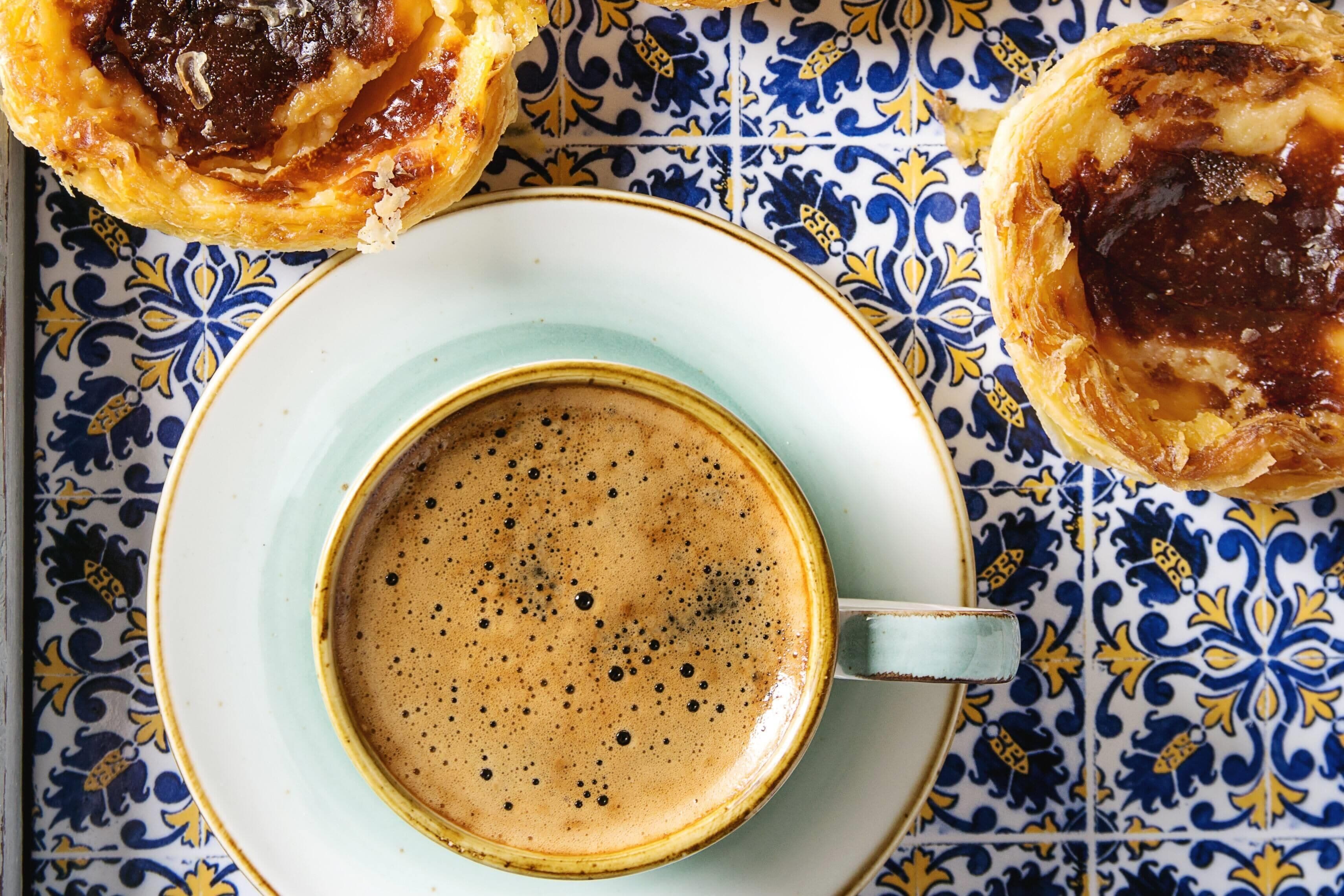 A cup of coffee on a plate with a blue and yellow patterned tablecloth.