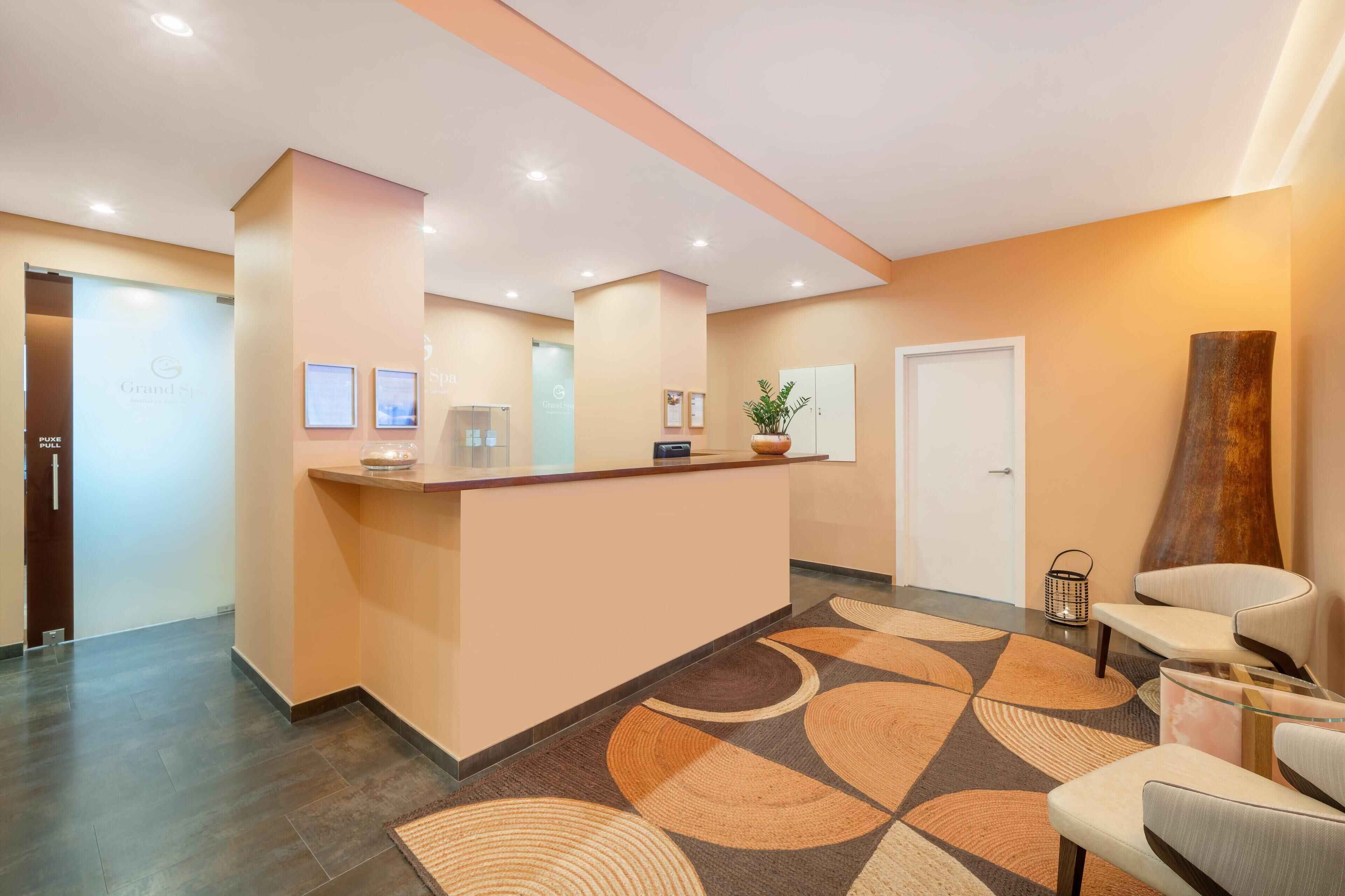A reception area with a counter, framed pictures, a potted plant, and a large vase.