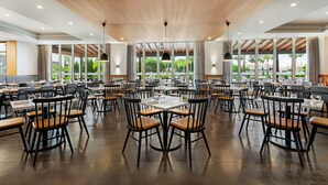 A spacious dining area with multiple tables and chairs, large windows offering views of greenery, and a wooden ceiling. - Wyndham Grand Algarve Quinta do Lago (Loulé)