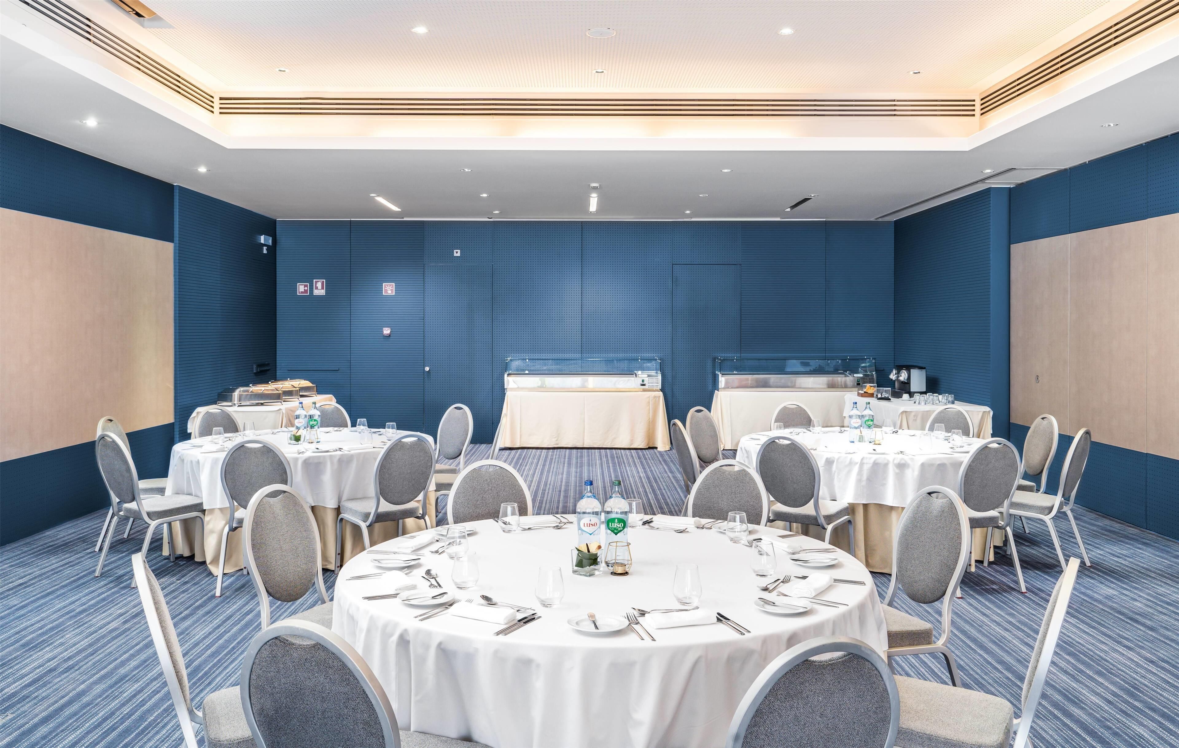 Una sala de conferencias con mesas redondas, sillas y una zona de bufé.