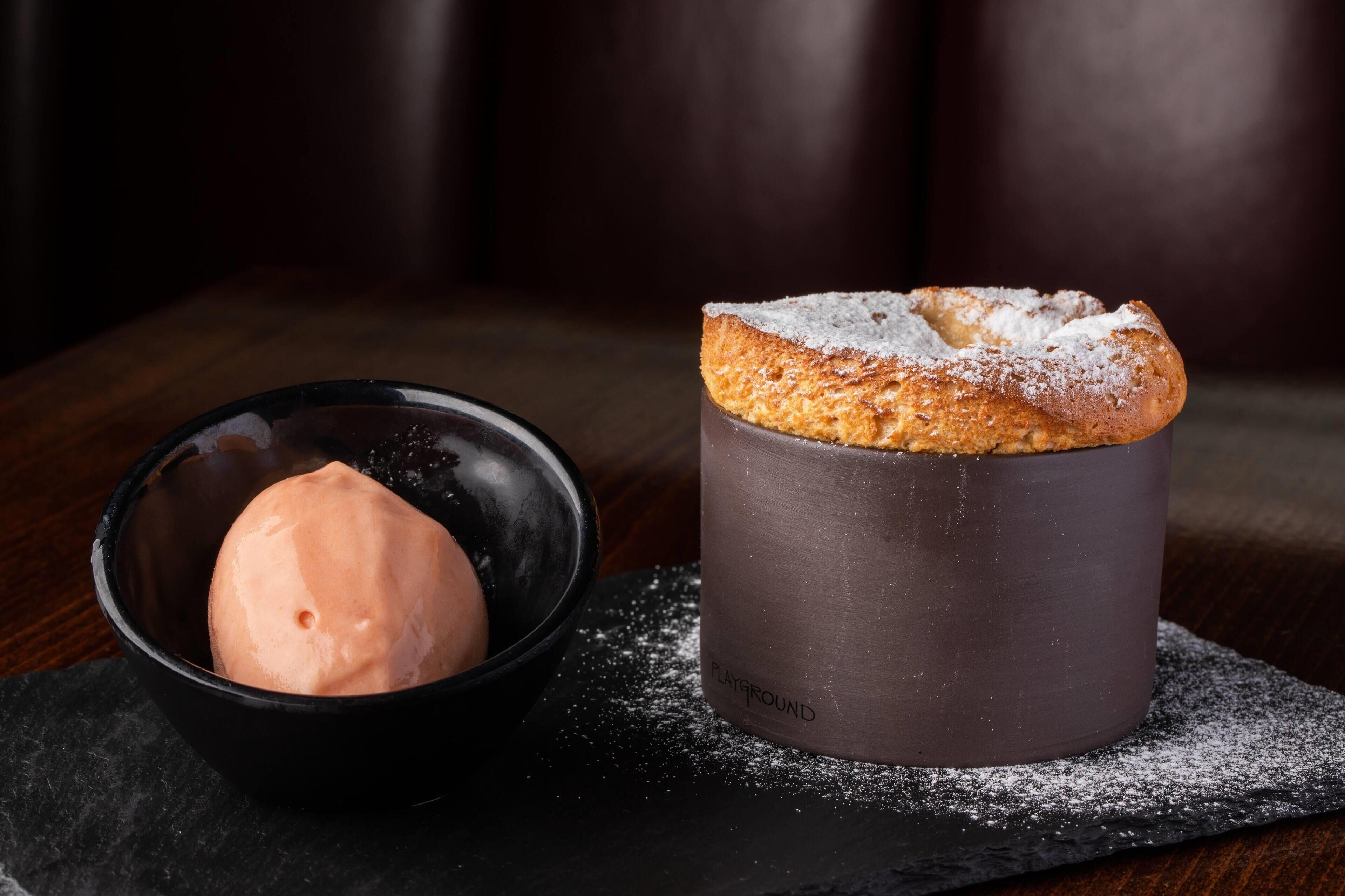 Un postre que incluye una bola de helado y un pastel espolvoreado sobre una bandeja de pizarra.