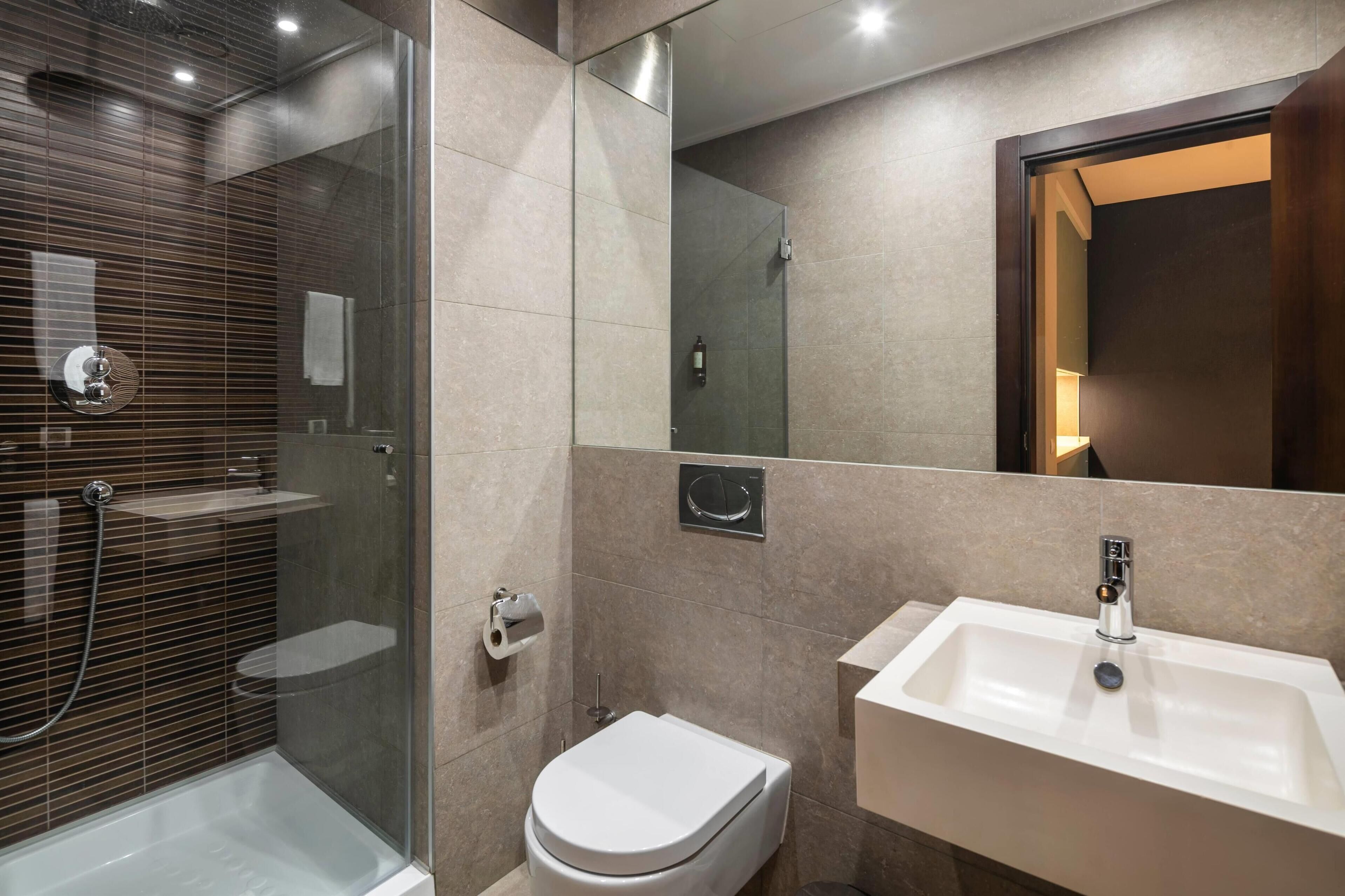 Een moderne badkamer met een douchecabine van glas, een wit toilet en een wastafel met een spiegel erboven.
