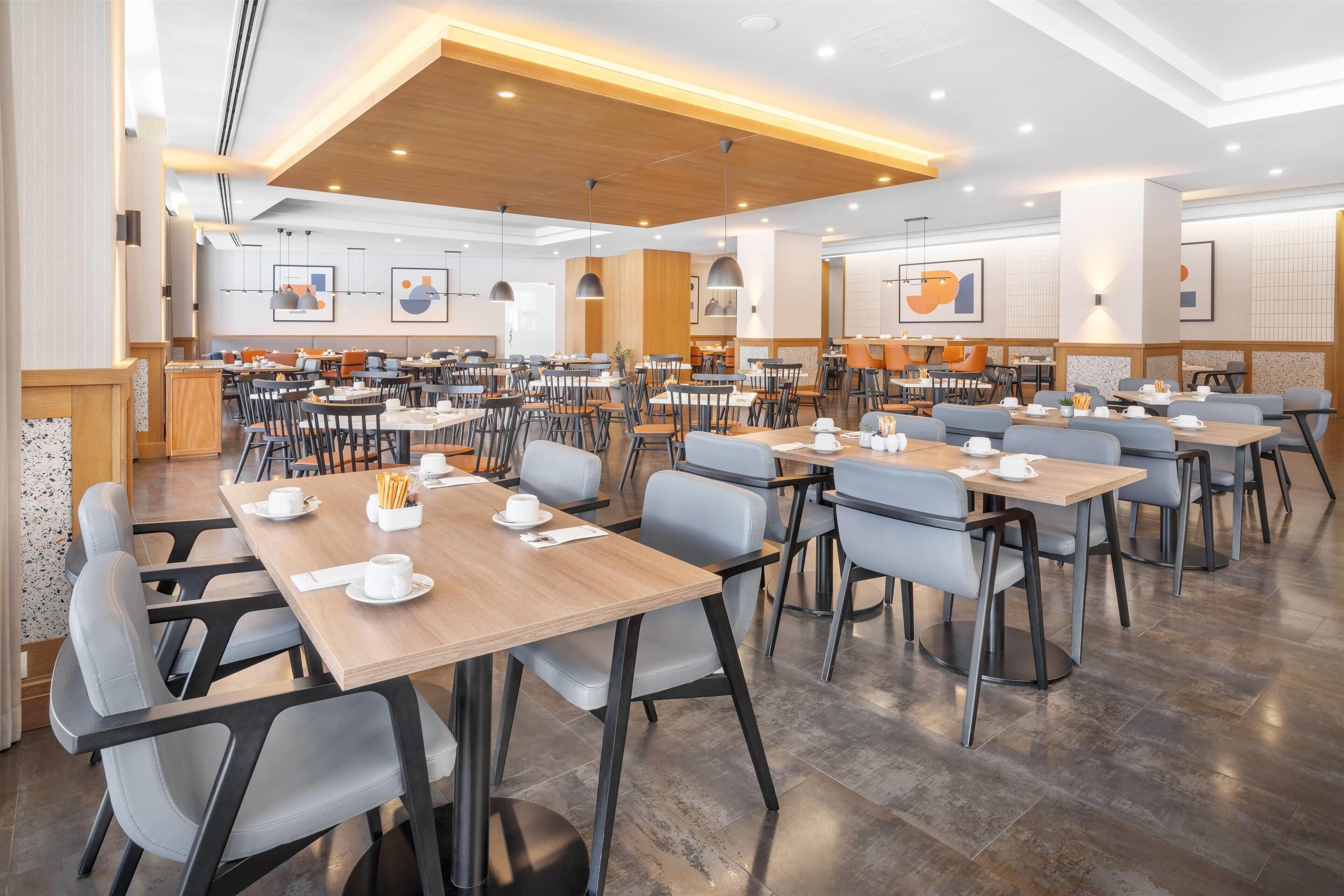 A spacious dining area with multiple tables and chairs, wooden ceiling panels, and wall-mounted artwork.