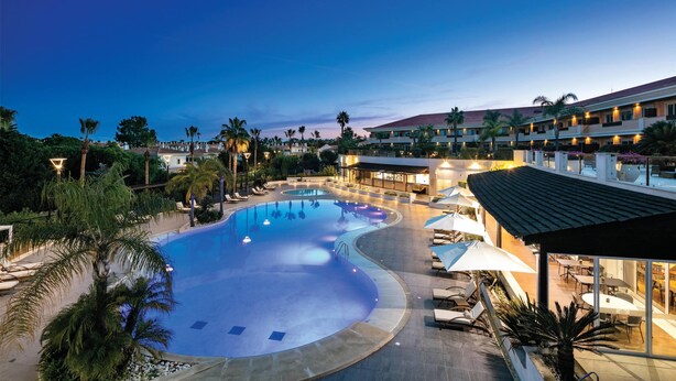 A resort pool area with lounge chairs, a swimming pool, and a building with multiple balconies. - Wyndham Grand Algarve Quinta do Lago (Loulé)