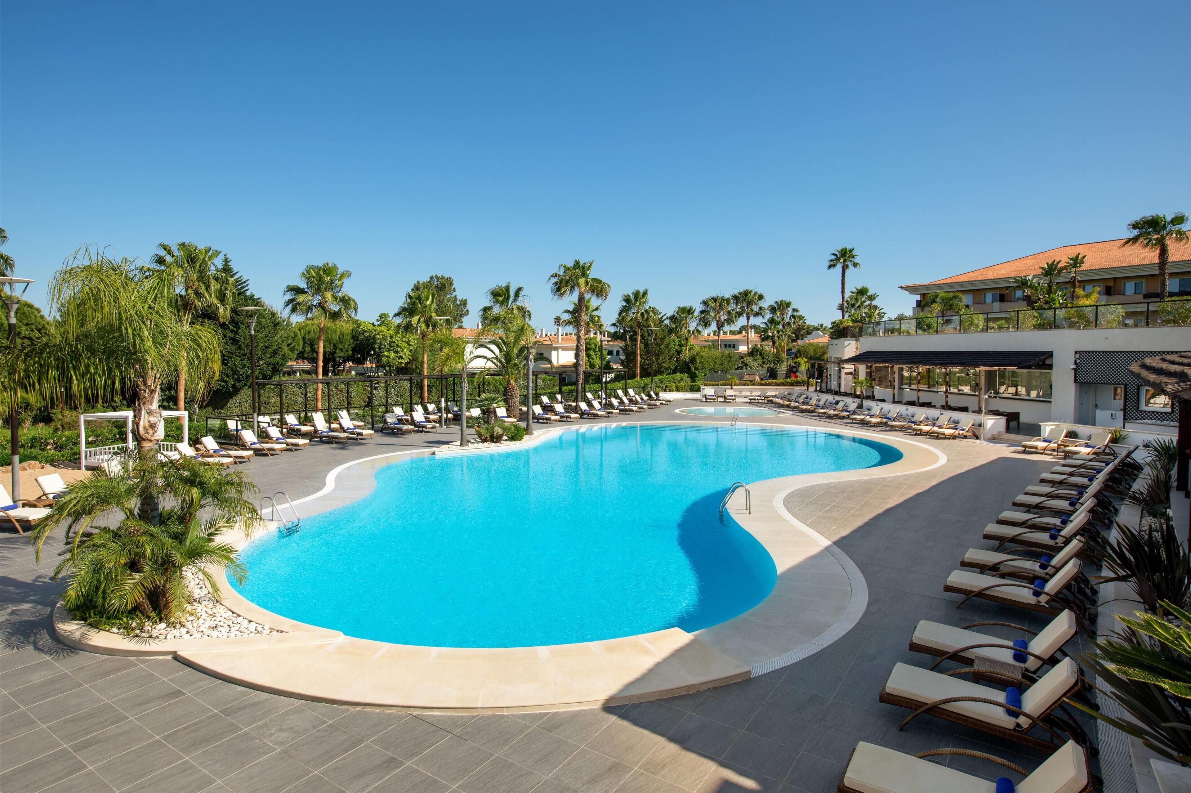 A resort pool with sun loungers and palm trees.