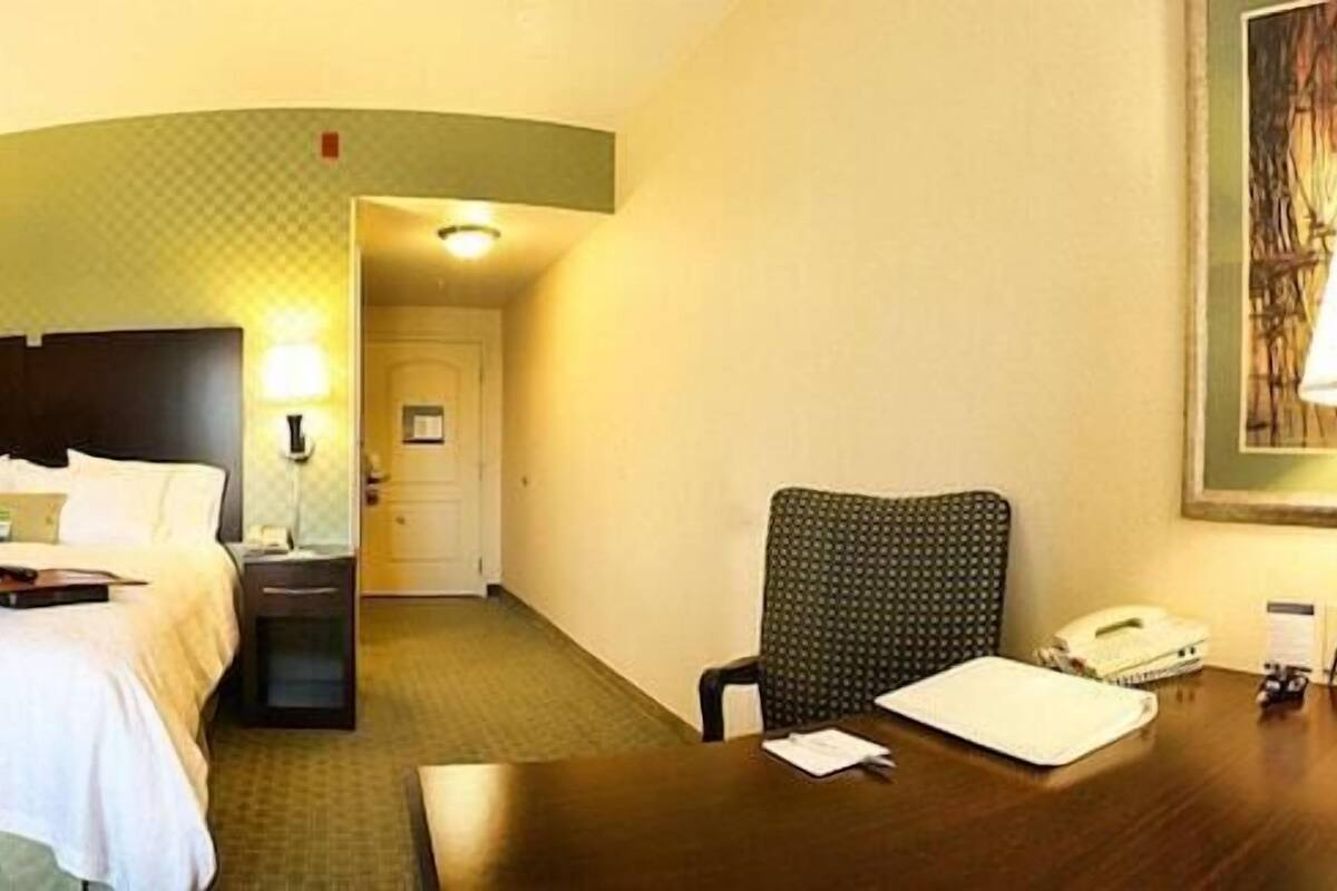 A hotel room with a bed, a desk, a chair, a television, and a painting on the wall.