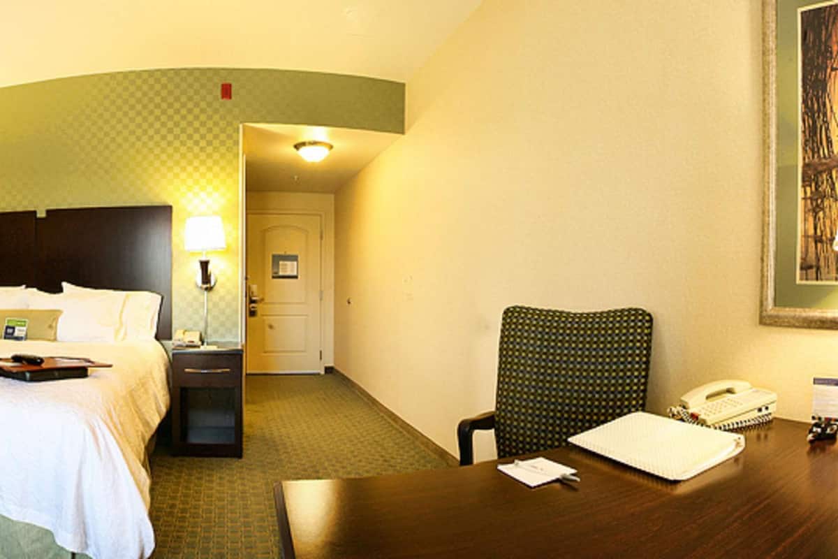 A hotel room with a bed, a desk, a chair, a television, and a lamp.