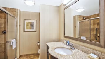 A modern bathroom with a glass-enclosed shower, a sink with a granite countertop, and a large mirror.
