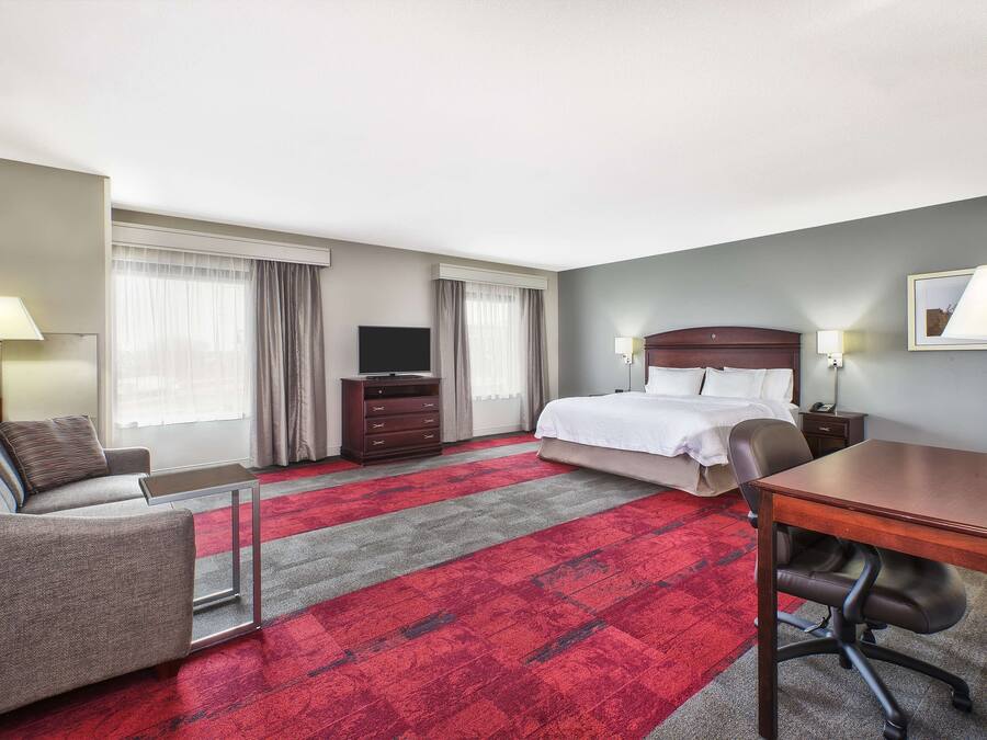 A hotel room with a bed, a desk, a chair, a sofa, a TV, and a dresser.