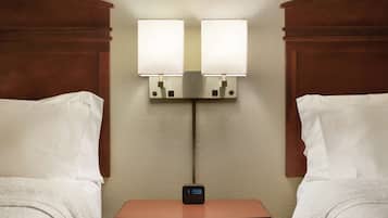 A hotel room with two beds, a nightstand with a digital clock, and wall-mounted lamps.